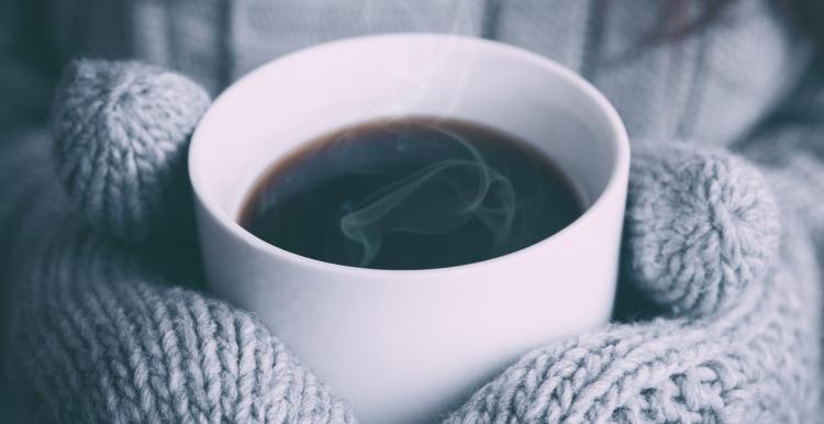 Person holding a hot cup of coffee wearing woolly gloves